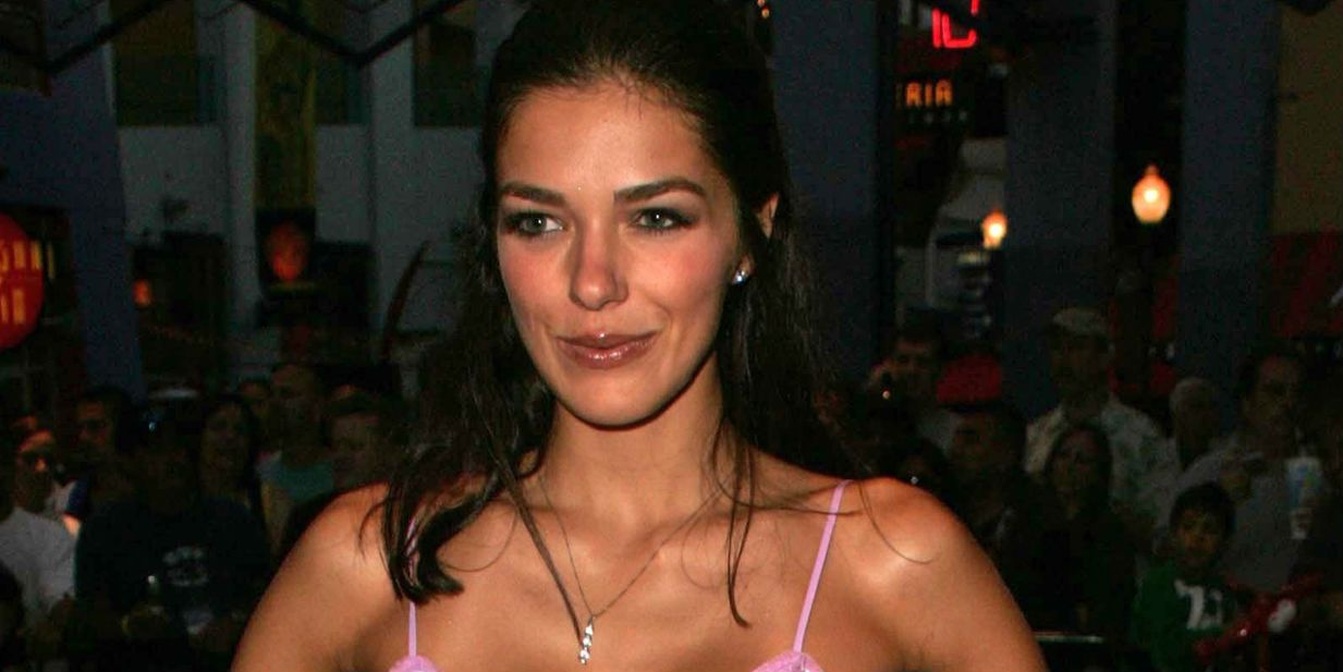 Model Adrianne Curry smiles with hair half up in a pink dress