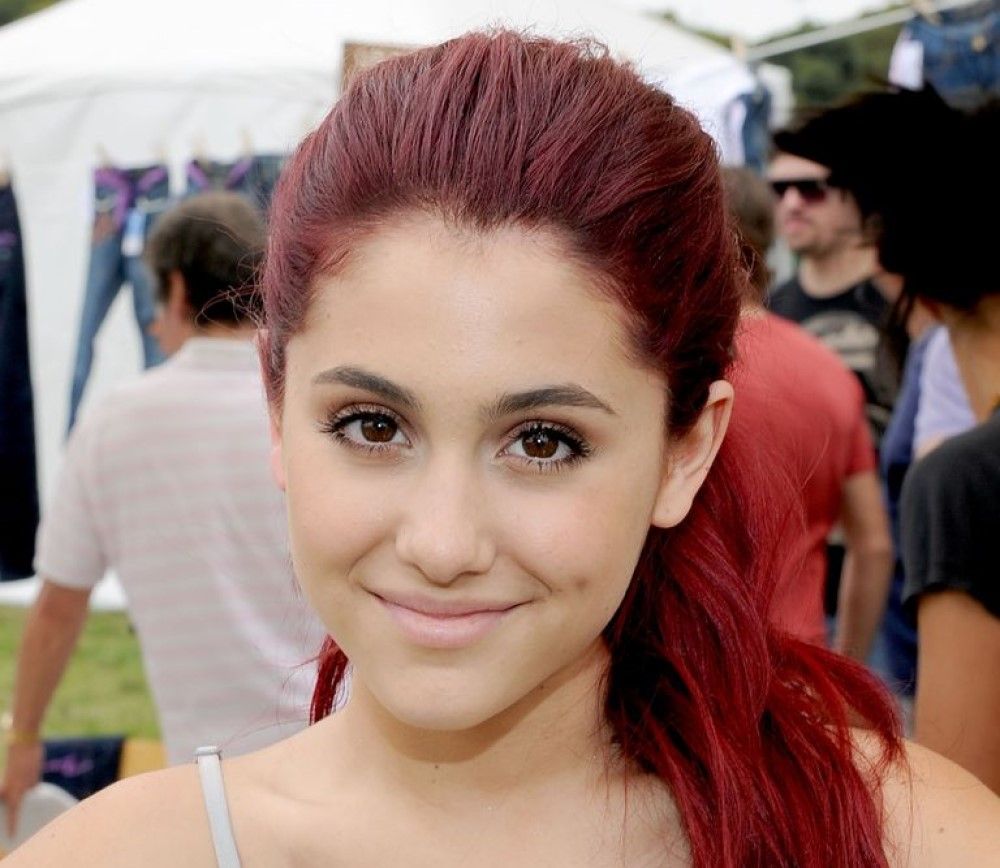 Ariana Grande with red hair on red carpet smiling with closed mouth