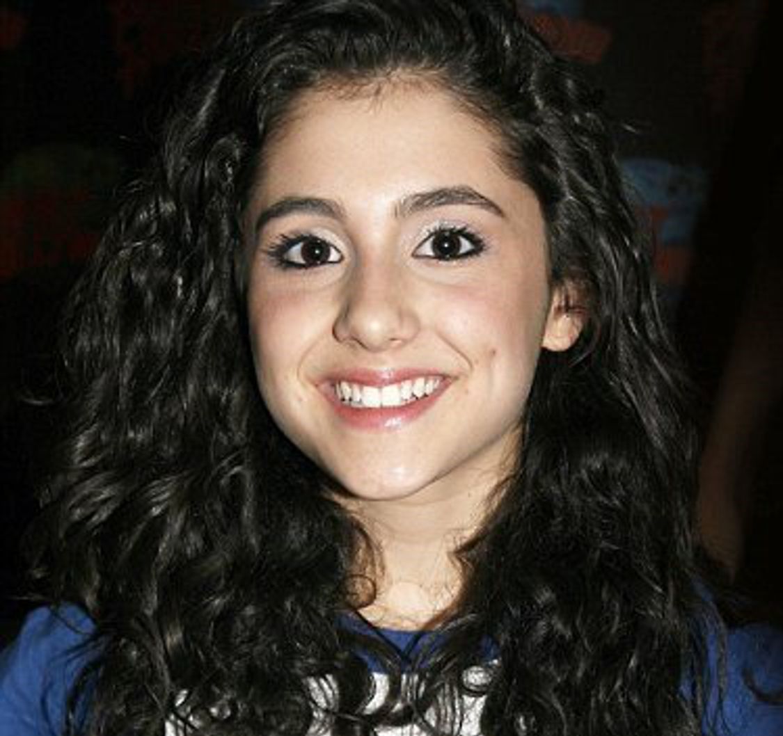 Young Ariana Grande smiling with dark curly brown hair in blue and white shirt
