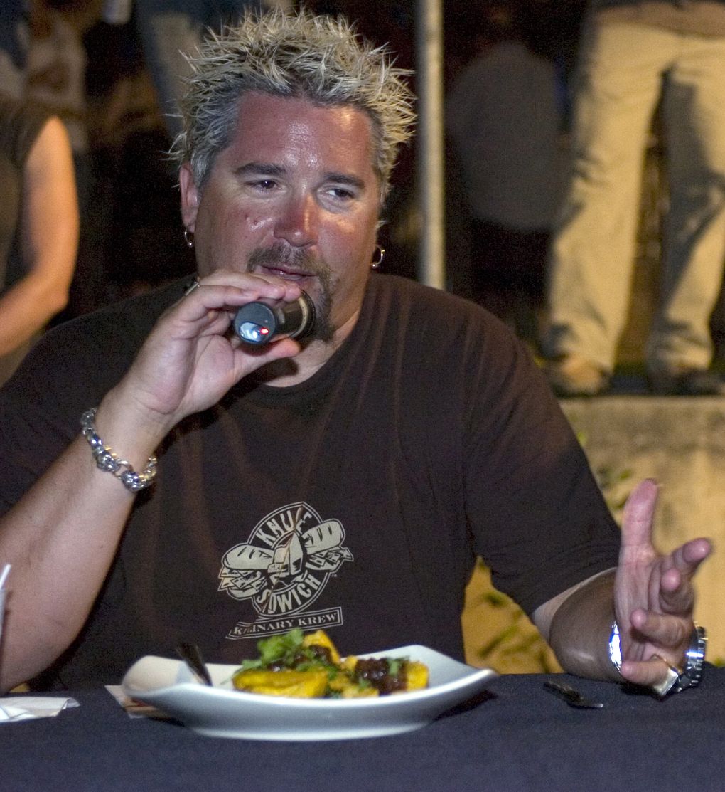 guy fieri sitting at table with food in front of him holding microphone