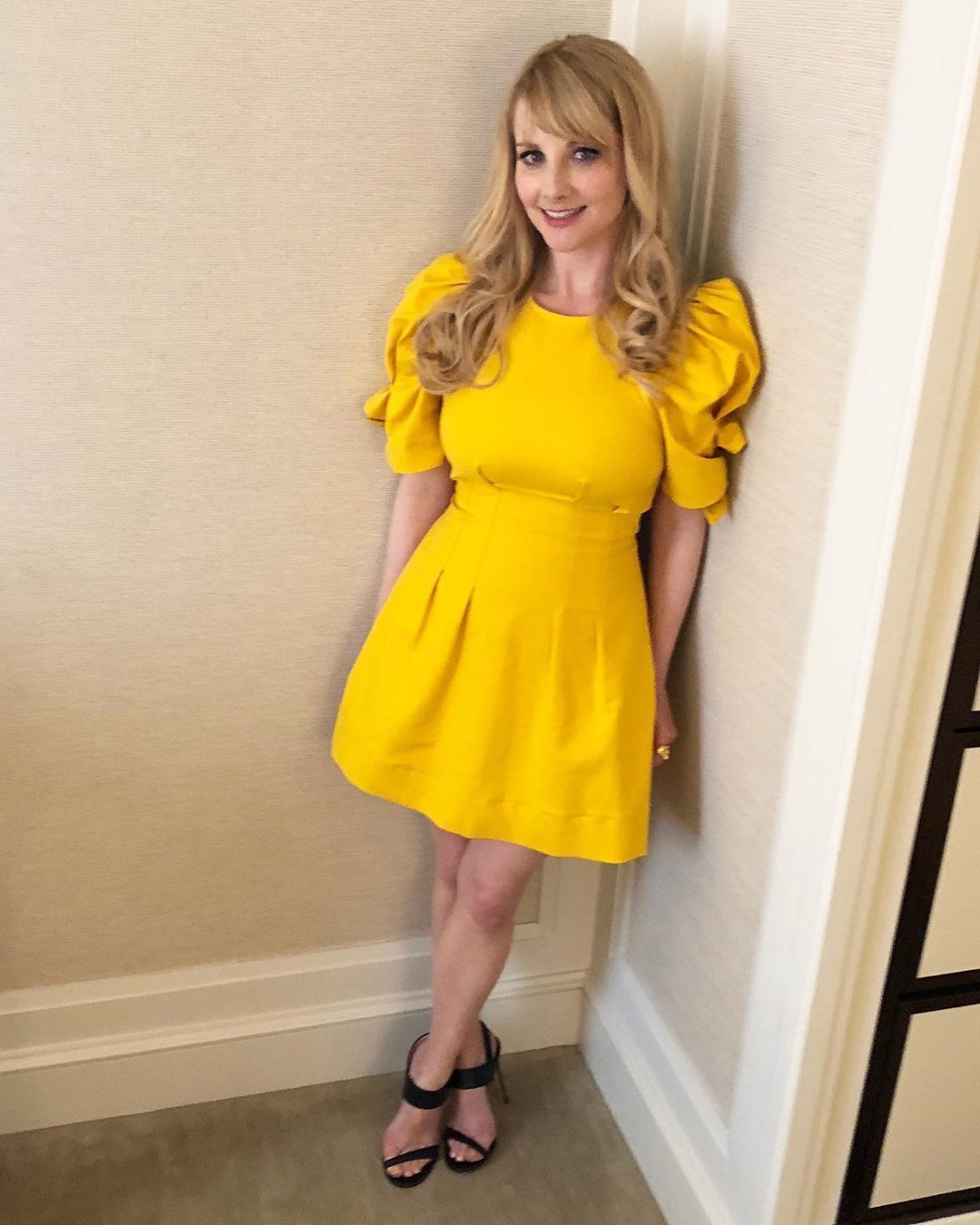 melissa rauch standing against wall wearing yellow dress