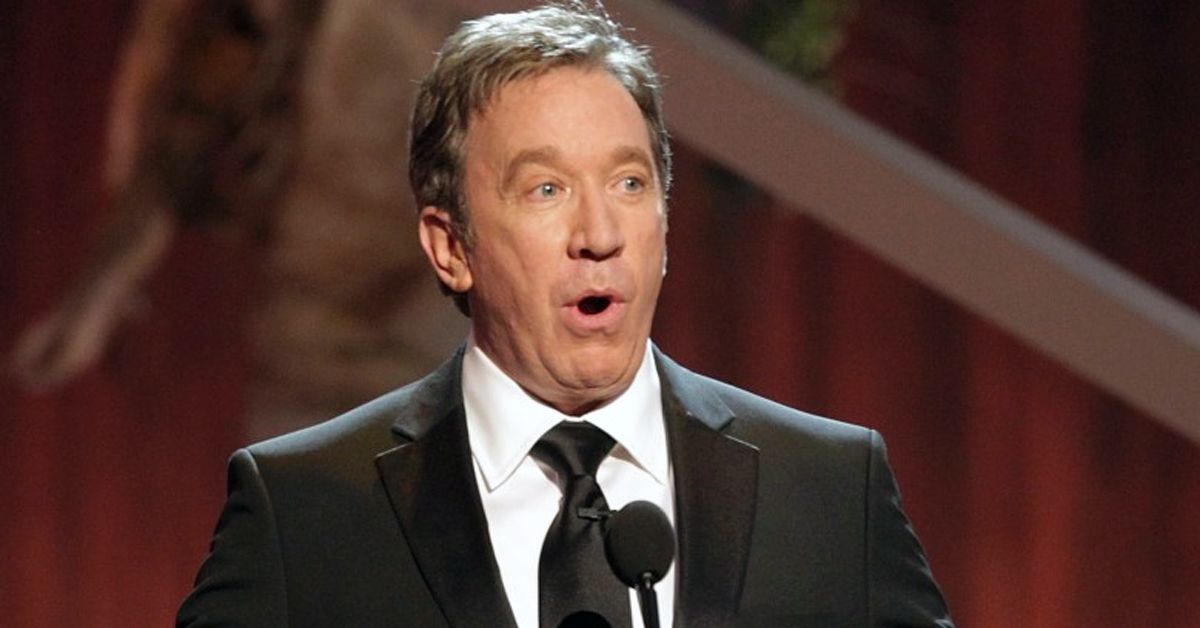 Tim Allen oops face suit and tie red curtain microphone