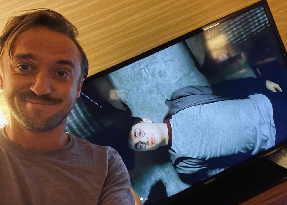 Tom Felton smiling in front of Harry Potter TV screen