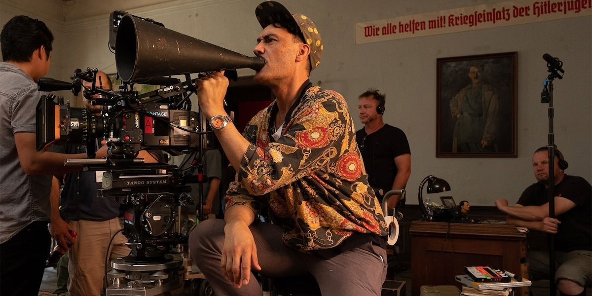 Taika Waititi speaking through a megaphone behind a camera on set