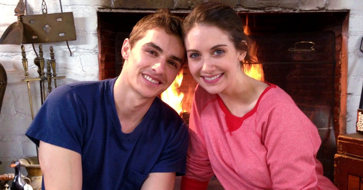 Dave Franco and Alison Brie sitting in front of a lit fireplace