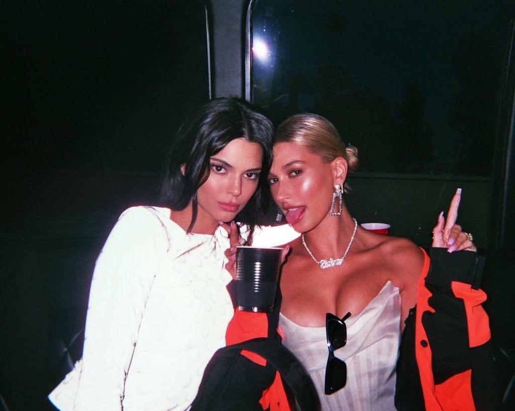 Kendall Jenner and Hailey Bieber tongue out drink dark club sitting