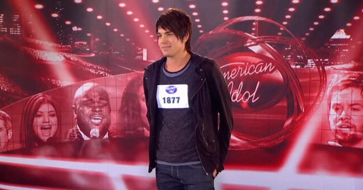Adam Lambert smiling at his American Idol audition and wearing a black hoodie, shirt, and pants.