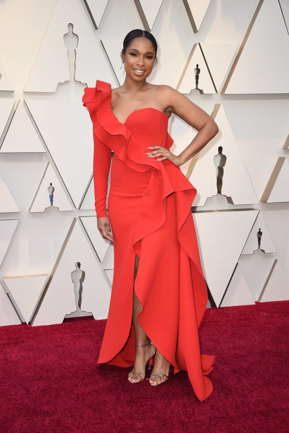 Jennifer Hudson wearing a coral colored dress and putting her hand on her hip at the Oscars.