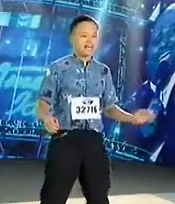 William Hung singing and dancing at his American Idol audition and wearing a blue button down shirt with black pants.