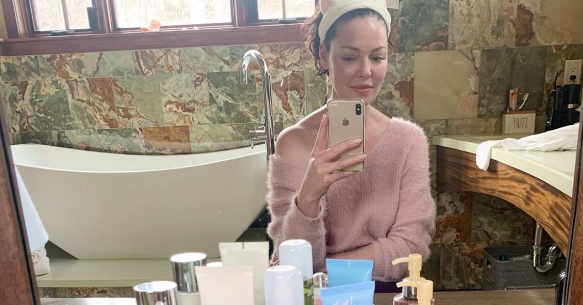 Katherine Heigl taking a picture with her phone in front of a mirror and her beauty products sitting in front of the mirror.