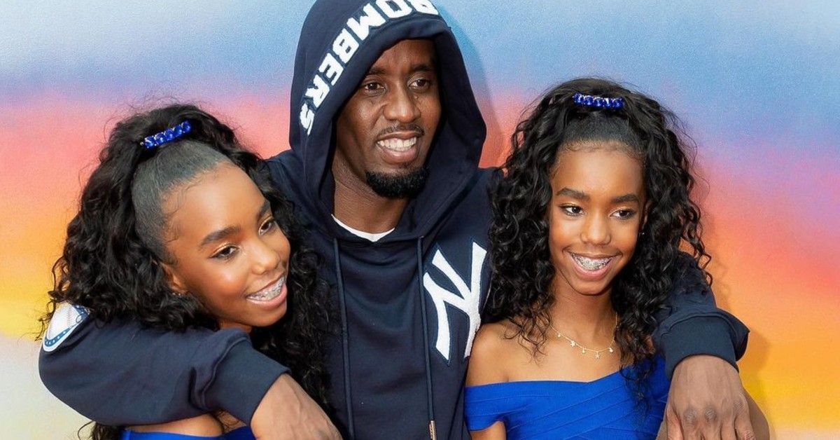 Diddy with arms around his twin daughters in front of rainbow background