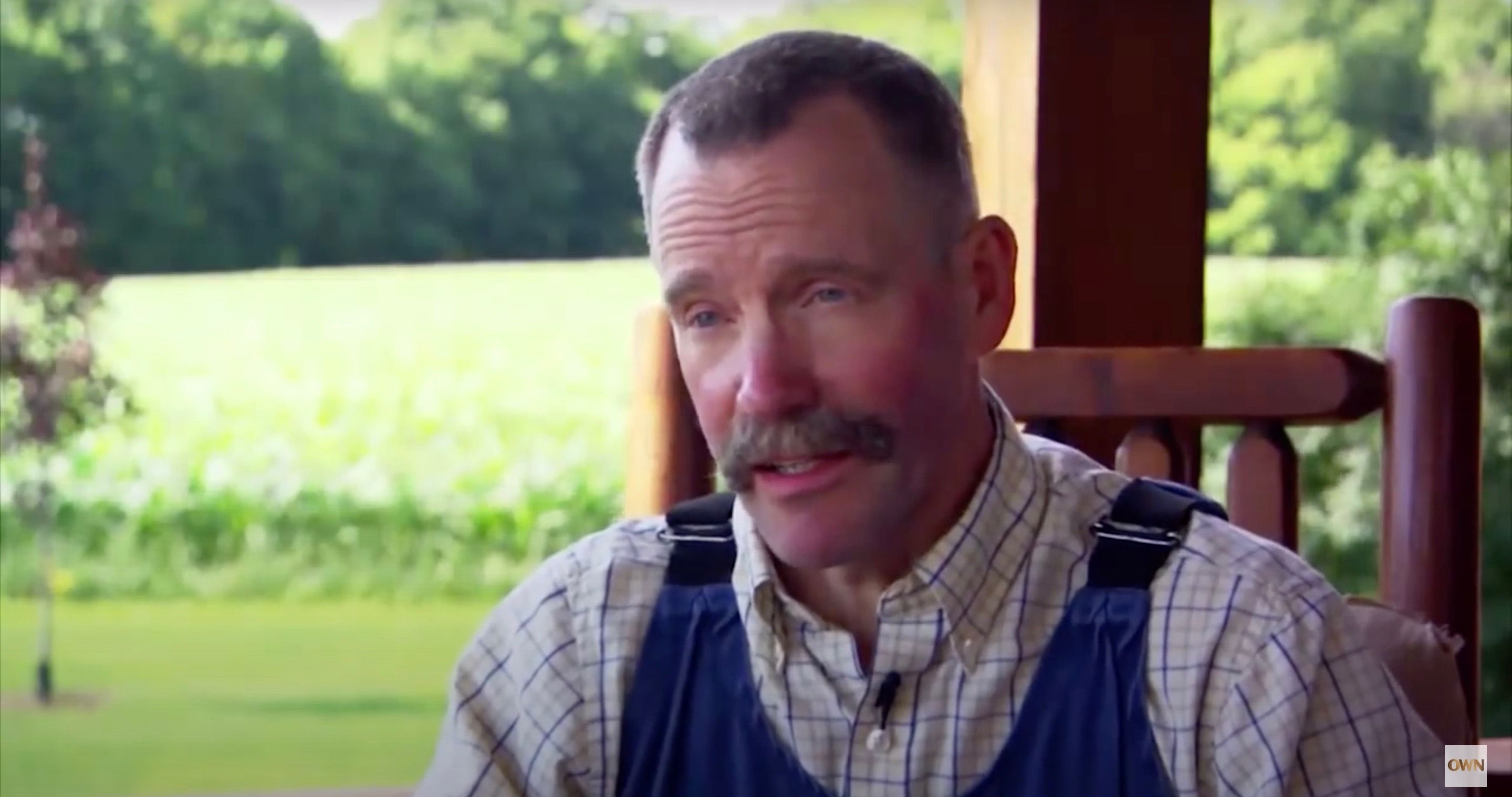Peter Ostrum wearing a plaid shirt with overalls on top and talking to Oprah.