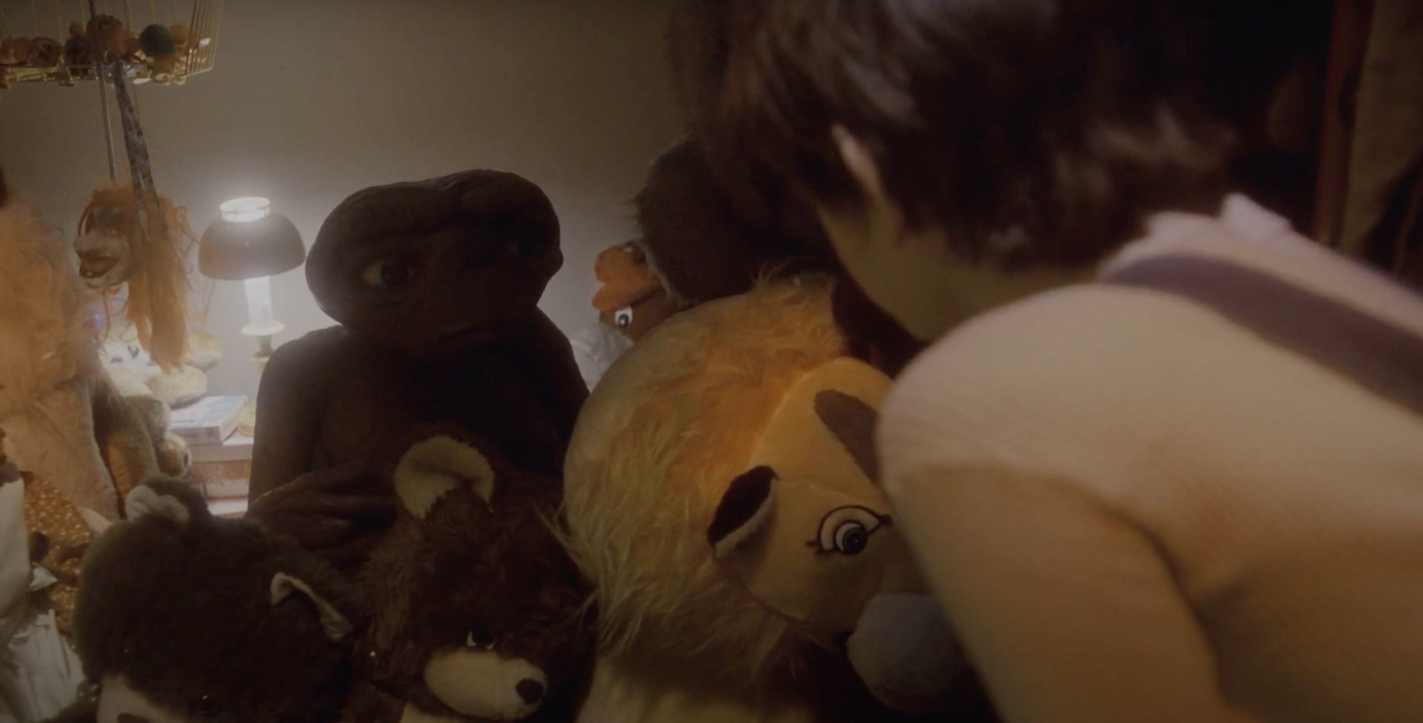 Camera shot of behind Elliott who's looking at E.T. who's sitting near stuffed animals.