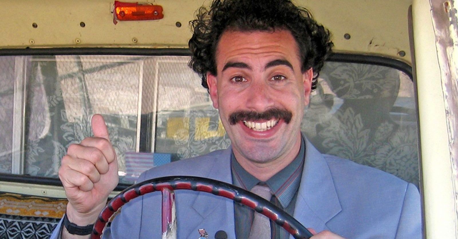 borat behind the wheel of a bus giving a thumbs up