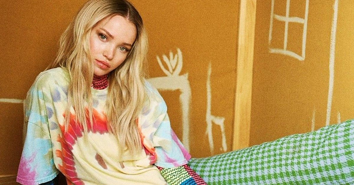 Dove Cameron in tie-dye shirt sitting in box house