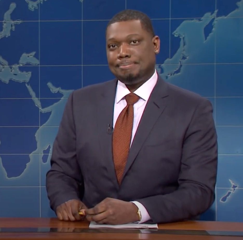 Michael Che sitting at a news desk on SNL.