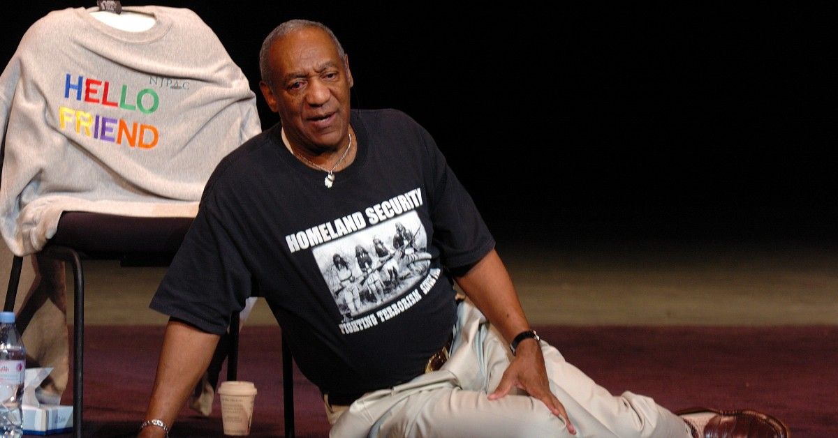 Bill Cosby in black shirt sits on ground