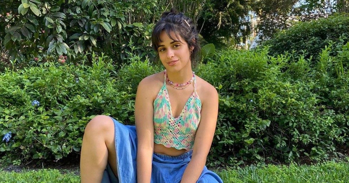 Camila Cabello posing in a garden with her hair up and a colourful top and blue skirt