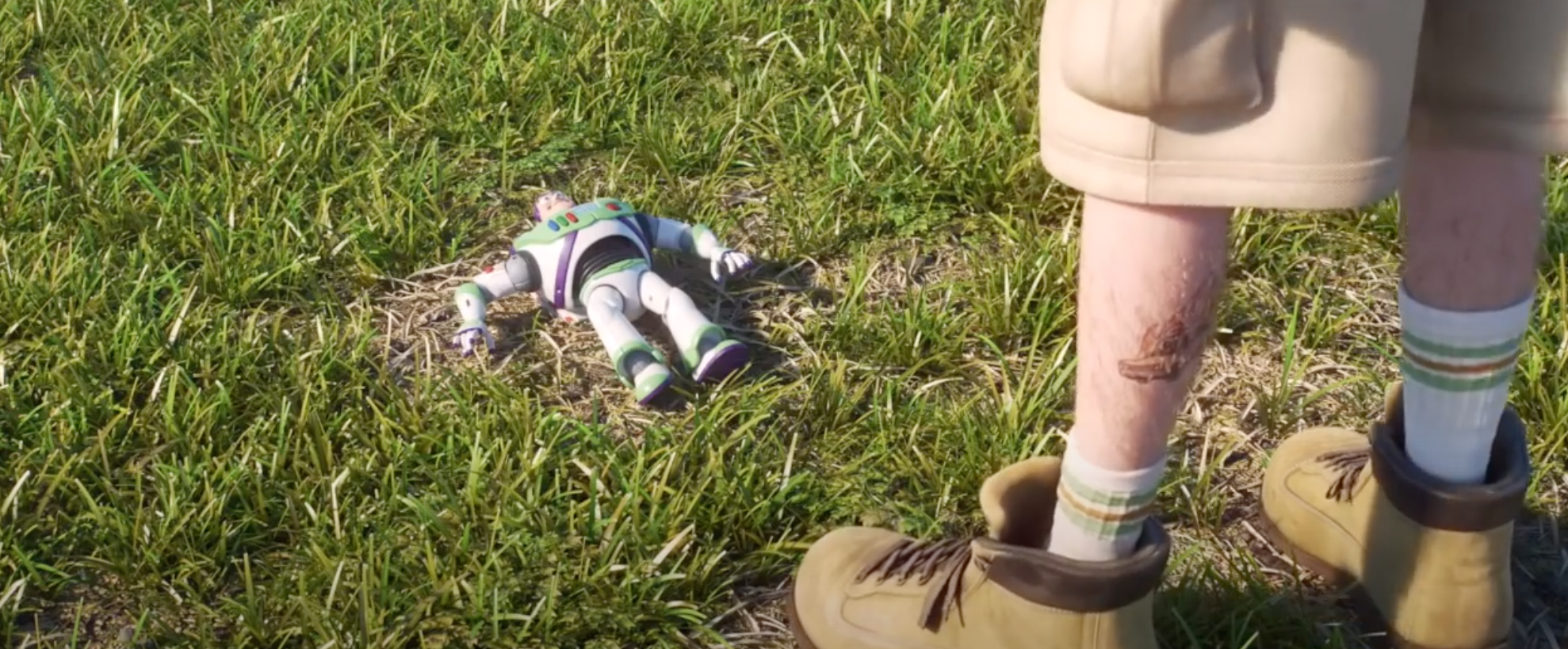 Buzz Lightyear laying in the grass and a man's legs with a tattoo of the Pizza Planet truck on the left one next to him in Toy Story 4.