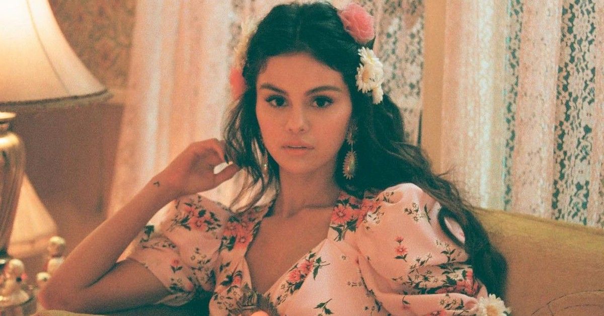 Selena Gomez sits on a couch with flowers in her hair in the cover for 