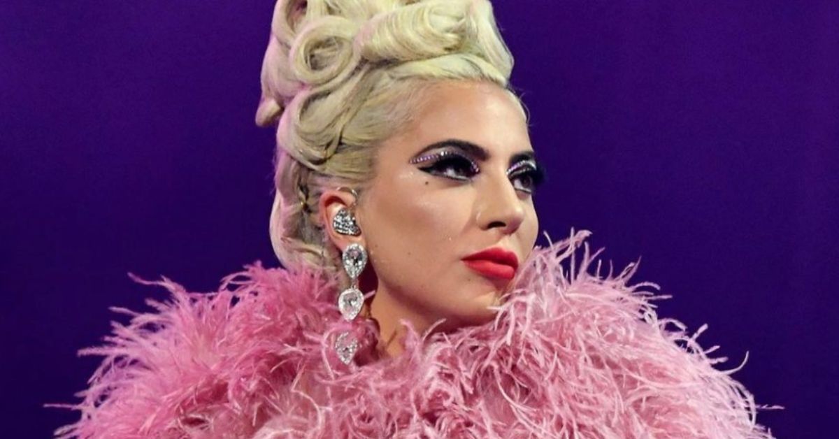 Lady Gaga wearing a pink feather boa in front of a purple wall