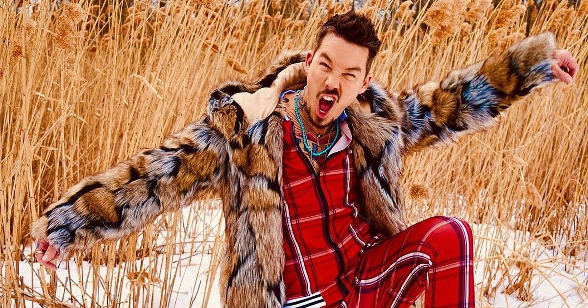 David Bromstad in fur jacket and red plaid suit poses in field of wheat