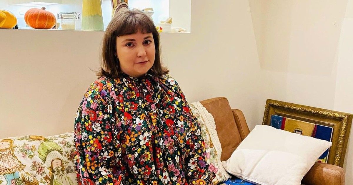 Lena Dunham in floral top sitting on couch in living area