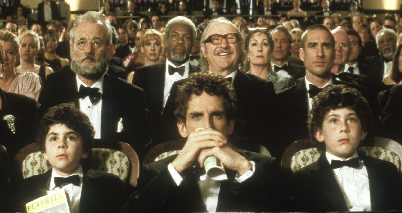 Several members of The Royal Tenenbaums cast, including Bill Murray, Danny Glover, Ben Stiller, Gene Hackman, Anjelica Huston, and Luke Wilson, wearing tuxedos in a still image from the Wes Anderson film