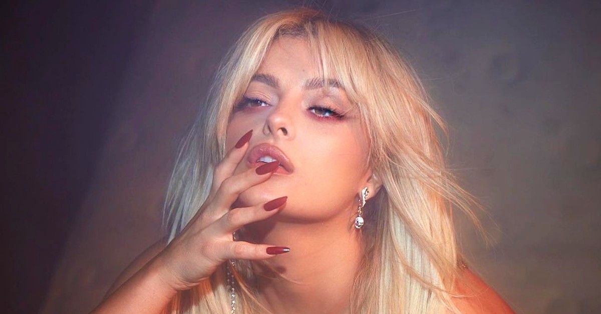Bebe Rexha with blonde hair, red nails and hand on face.