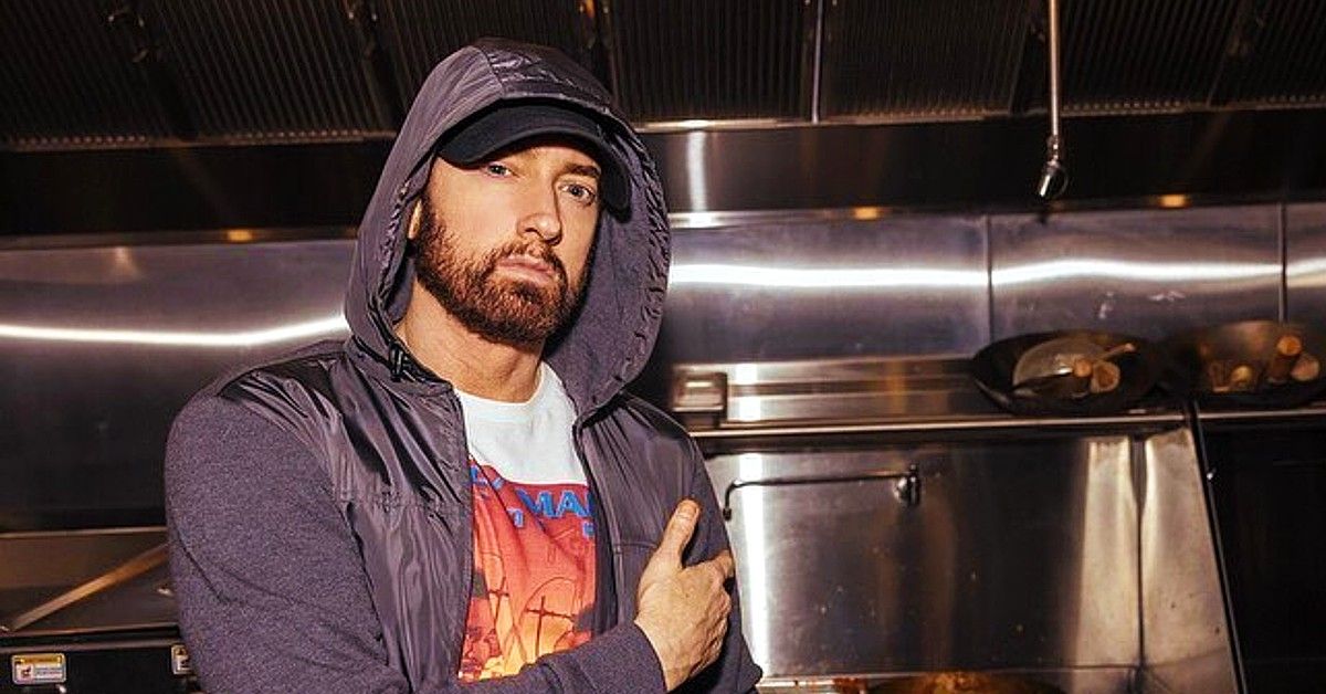 Eminem in gray hoodie stands in stainless steel kitchen