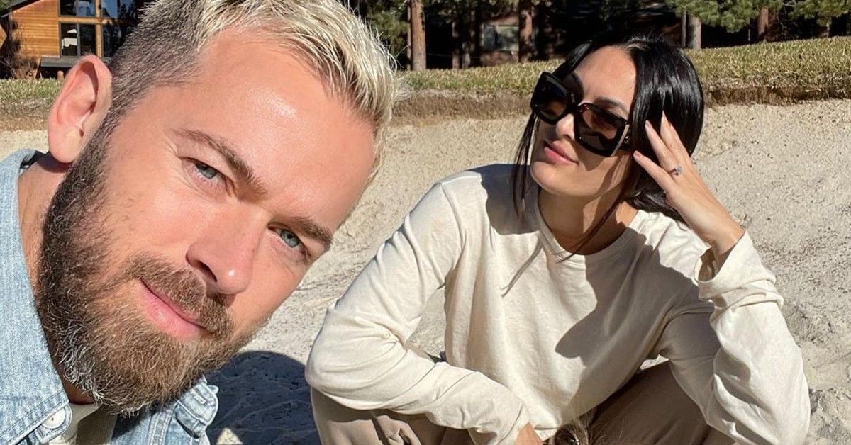 Artem Chigvintsev takes selfie with Nikki Bella in a tan shirt while sitting on the beach