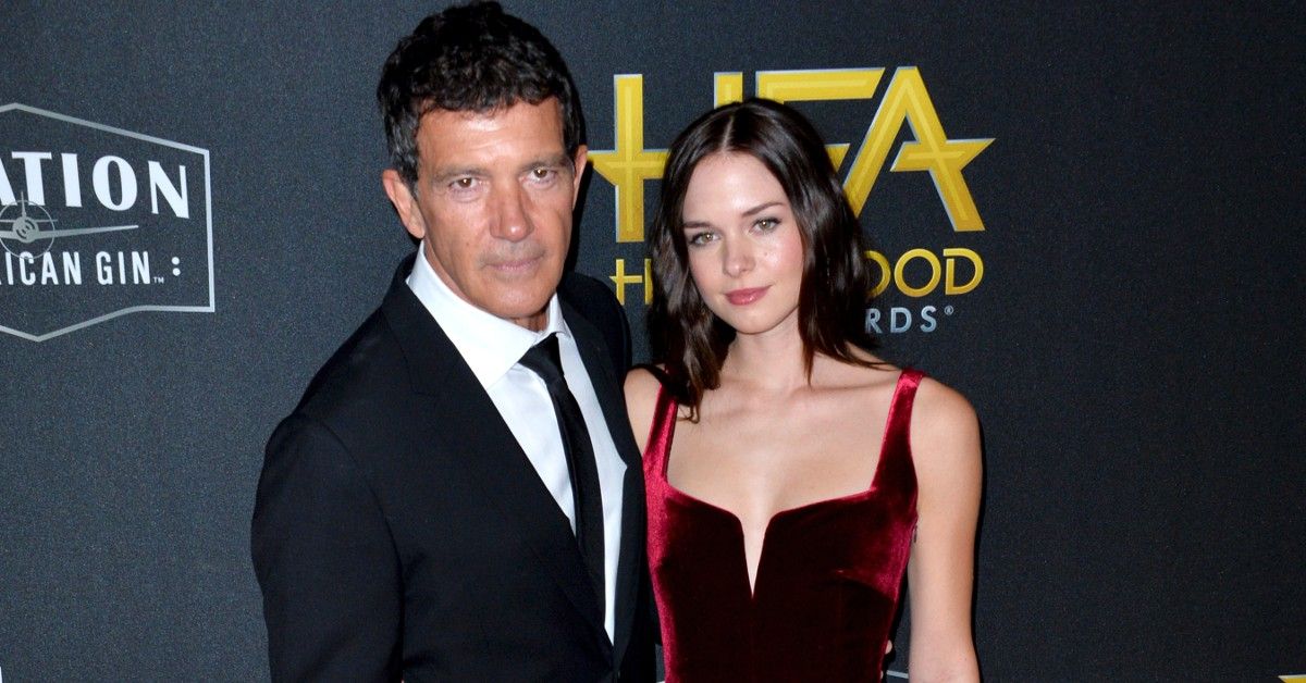 Antonio Banderas in black and white tuxedo stands next to daughter Stella in red dress against black background for red carpet event