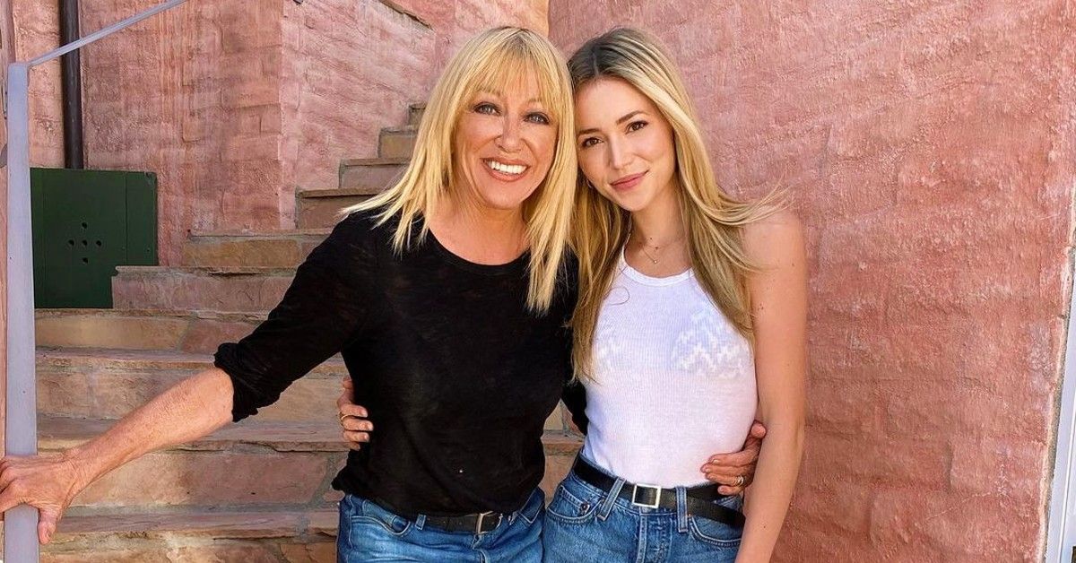 Suzanne Somers in black top poses next to grandaughter Camelia on stairs outside