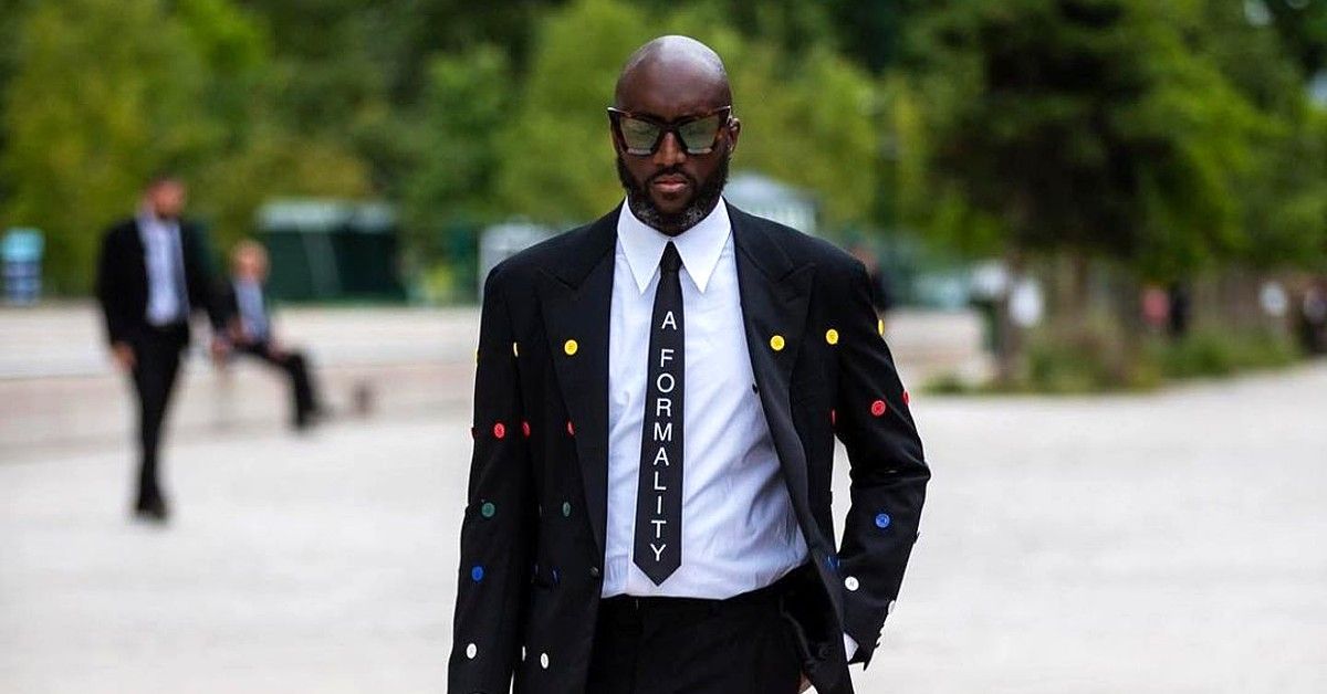 Virgil Abloh walking down sidewalk in black and white suit with colored polka dots and a black tie that says A Formality