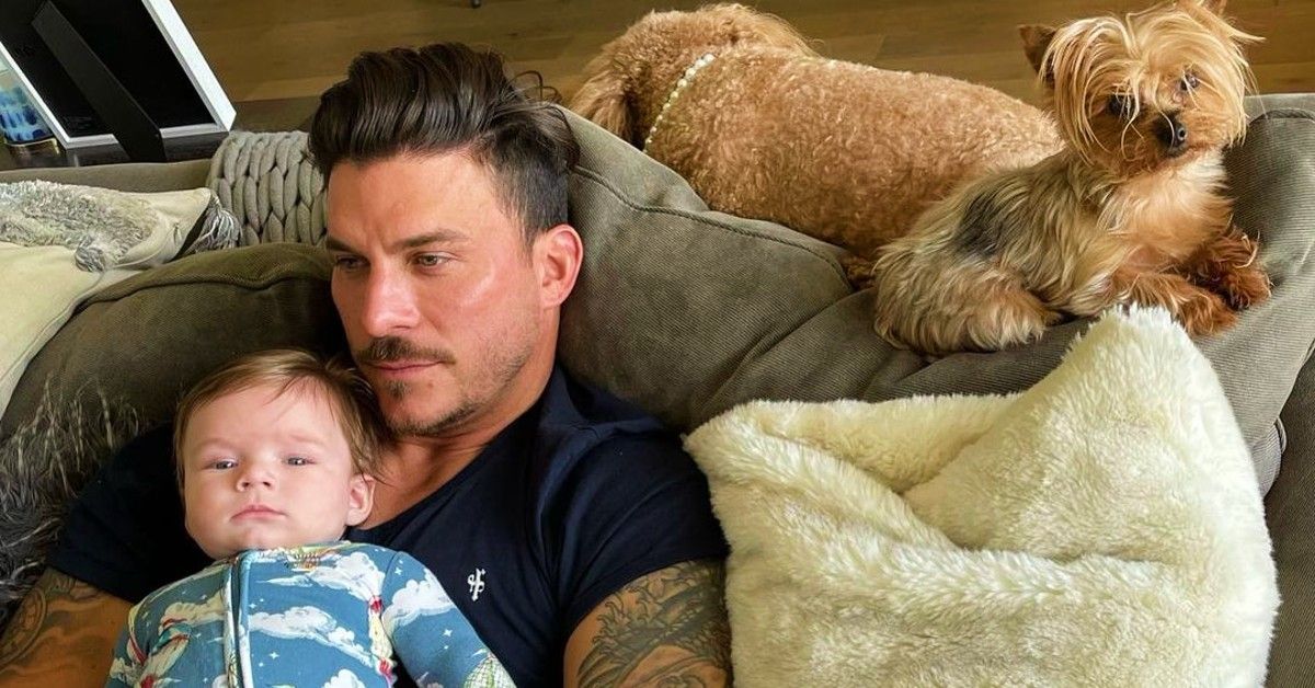 Jax Taylor sitting on couch holding his son, Cruz, with dogs near by in living room
