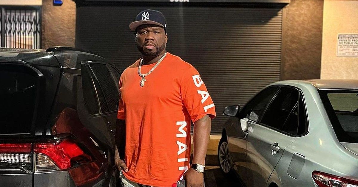 50 Cent in orange shirt stands by cars