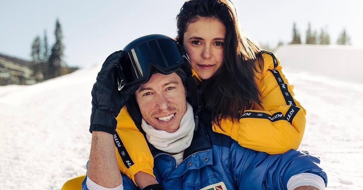 Nina Dobrev with her arms around boyfriend Shaun White, both wearing winter gear and posing on a snowy hill