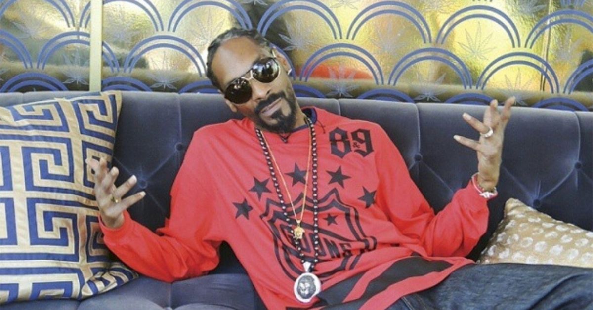 Snoop Dogg posing on couch wearing a red shirt.