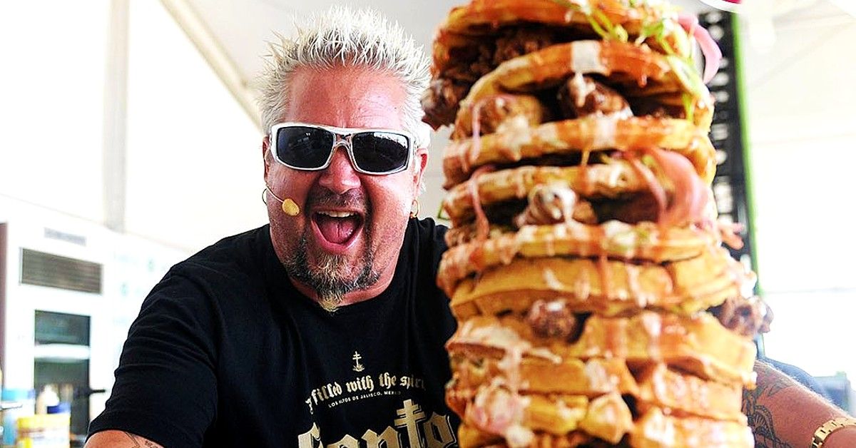 Guy Fieri posing behind large burger stack