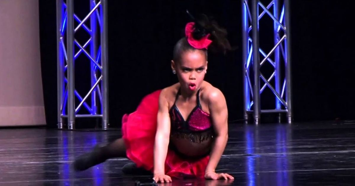 A young girl is performing on stage wearing a black and red costume and rocking her hair in a high ponytail.