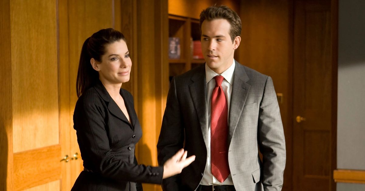 Sandra Bullock and Ryan Reynolds in suits in the office.