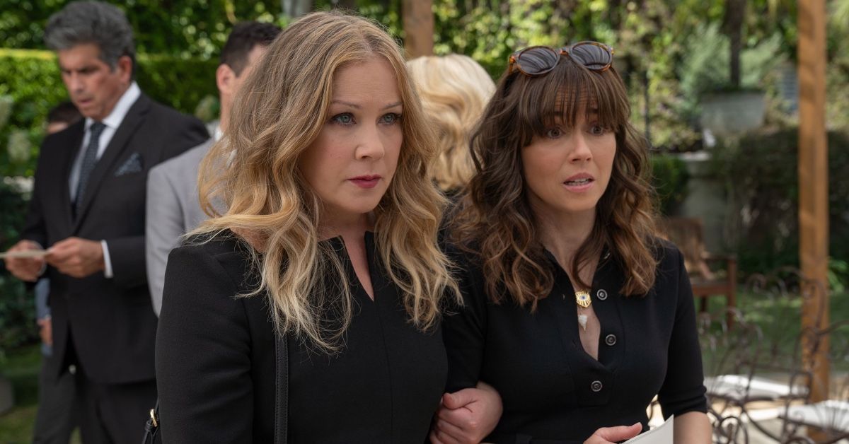 Christina Applegate and Linda Cardellini as Jen Harding and Judy Hale in a scene of Dead to Me season three. The characters are standing arm in arm and are wearing black outfits, with Judy looking particularly alarmed.