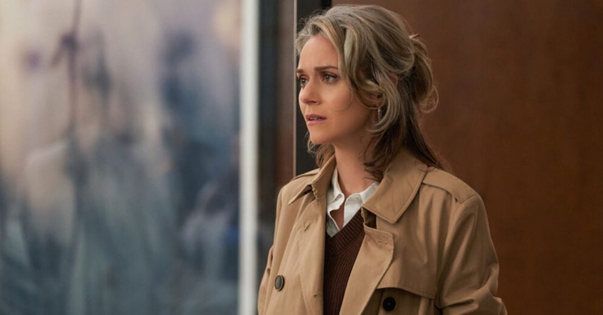 Actress Hilarie Burton as Gretchen Taylor in a scene of Good Sam. She has silver hair pulled back in a half ponytail and is wearing a trench coat over a brown waistcoat and white shirt. She's looking sad.