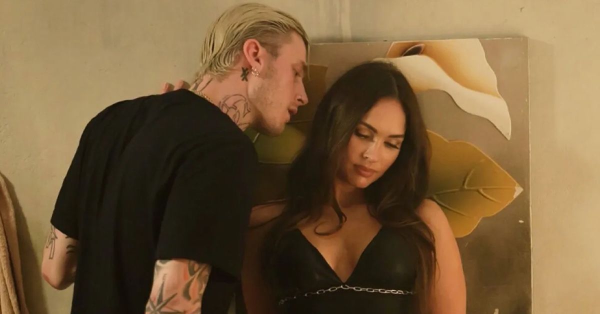 Machine Gun Kelly (Colson Baker) in the role of Calvin and Megan Fox in that of Rebecca Lombardo in Midnight in the Switchgrass. He's whispering something in her ear as she leans against the wall.