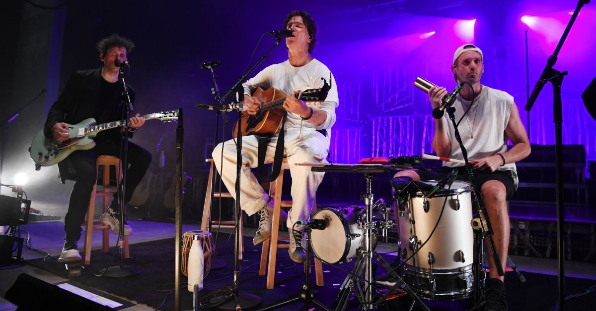 Band members of Third Eye Blind sitting on stools and performing at a concert