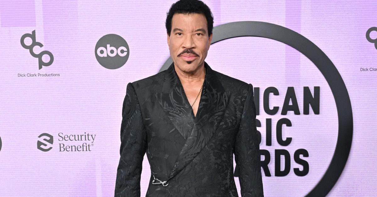 Lionel Richie standing on the red carpet against a purple background