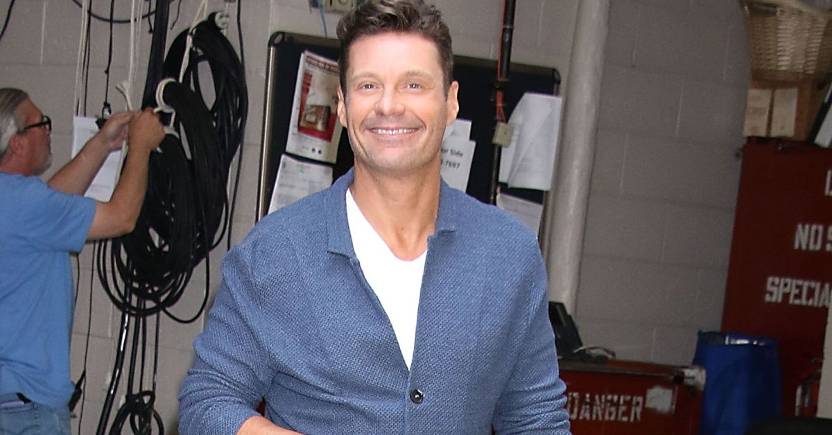 Ryan Seacrest standing wearing a blue suit and smiling