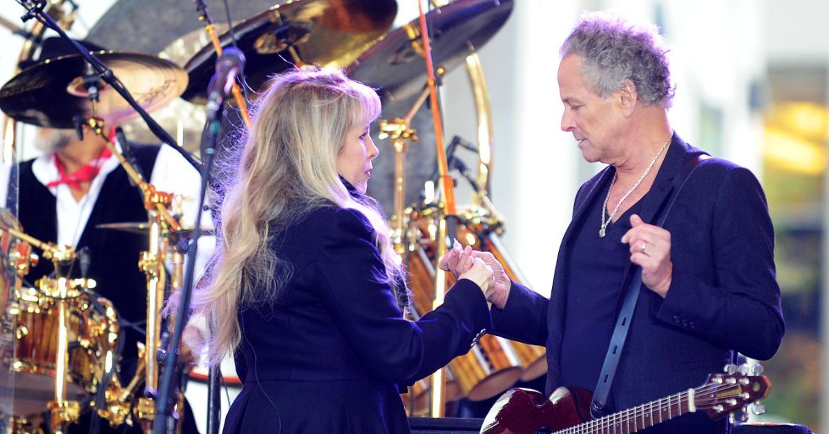 Lindsey Buckingham and Stevie Nicks holding hands and looking at each other while performing with Fleetwood Mac.