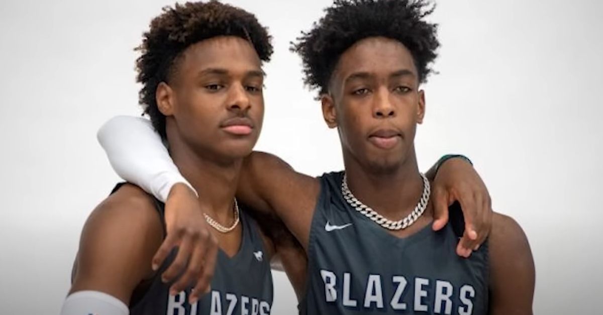 Zaire and Bronny holding each other while they pose in Blazers jerseys