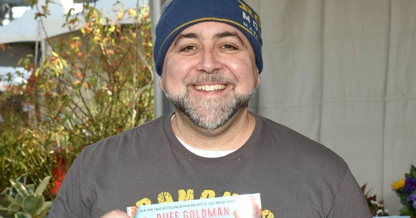 Duff Goldman smiling and holding up his cookbook